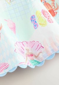 Sirena con capelli bianchi e coda verde dentro una grande conchiglia rosa su tessuto con illustrazioni di conchiglie e aragoste, bordo blu smerlato.