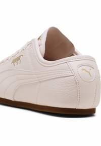 Jasnoróżowe sneakersy Puma z teksturowaną skórzaną cholewką, złotymi akcentami logo i brązową gumową podeszwą, z ozdobnym sznurowaniem.