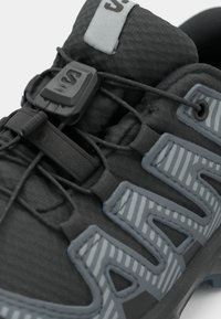Schwarzer Sportschuh mit grauen Akzenten, ausgestattet mit einem strukturierten Obermaterial, elastischen Schnürsenkeln und einer geformten Ferse für Stabilität.