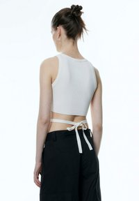 Witte geribbelde crop top met een ronde halslijn en achterste strikjes, gecombineerd met zwarte loszittende broek. Glad textuur, minimalistisch design.