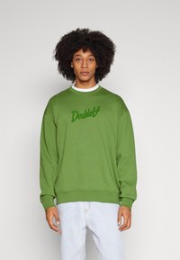 Felpa verde realizzata in morbido tessuto, con scollo rotondo e un logo ricamato testurizzato sul petto. Vestibilità casual con polsini a costine.