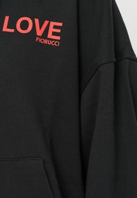 Crni dukserica od tkanine s crvenim natpisom "LOVE FIORUCCI" na prsima i prednjim kengurskim džepom vidljivim na dnu.