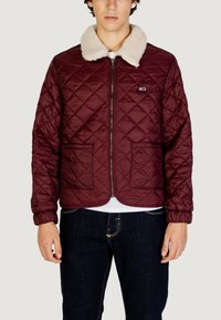 Giacca matelassé color granata con colletto in ecopelliccia color crema, chiusura frontale con cerniera e due tasche anteriori, con polsini e orlo a coste.