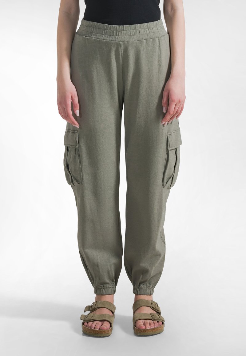 Lekkie, oliwkowozielone spodnie typu cargo z elastycznym paskiem w talii, zwężane u dołu nogawek i dwoma bocznymi kieszeniami. Noszone z brązowymi sandałami.