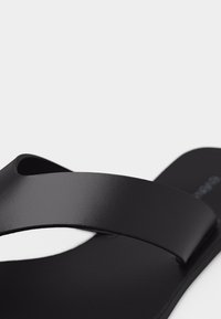 Μαύρη σαγιονάρα με πλατιά, λεία λουρί και ανάγλυφο πέλμα, εμφανίζεται σε λευκό φόντο.