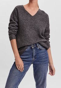 Maglione a V color grigio carbone con trama a coste, maniche arrotolate e vestibilità comoda, abbinato a jeans denim blu a vita alta.