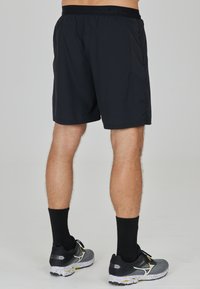 Schwarze Sportshorts mit elastischem Taillenbund und Seitentaschen, mit kontrastierenden Texturdetails, kombiniert mit schwarzen und grauen Laufschuhen.