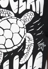 Black t-shirt featuring a large white graphic of a sea turtle, detailed shell patterns, with additional white accents and text around it.