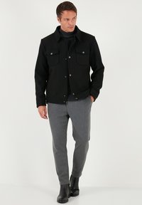 Juoda striukė su dviem krūtinės kišenėmis, spaudėmis ir apykakle, derinama su pilka pritaikyta kelnėmis ir juodais kulkšnies batais.