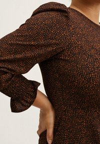 Braunes strukturiertes Kleid mit einem Puffärmel und gerafftem Manschettenabschluss, verziert mit einem verstreuten Punktmuster in Orangetönen.