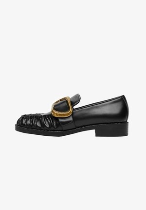 Mocassin en cuir noir avec devant froncé, grosse boucle dorée sur la bride, et talon bas empilé, vue de côté.