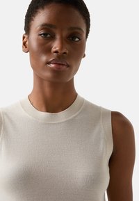 Hellbeiges ärmelloses Stricktop mit glatter Textur, rundem Ausschnitt und feinen Rippenstrickdetails am Hals- und Armausschnitt.