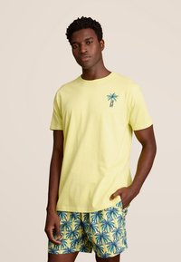 Geel katoenen T-shirt met een palmbomontage en blauwe accenten, gecombineerd met gele shorts met een palmbomenpatroon. Gladde textuur.
