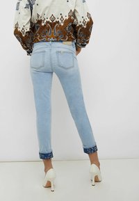 Světle modré úzké džíny s ohrnutým lemem, které mají modrý vzorovaný akcent. Materiál je denim s hladkou texturou a minimálním opotřebením.