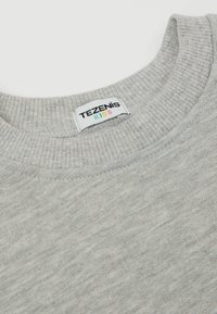 Helles graues Sweatshirt mit geripptem Kragen. Das Etikett lautet "TEZENIS KIDS" mit bunten Buchstaben auf weißem Hintergrund. Weiche Textur.