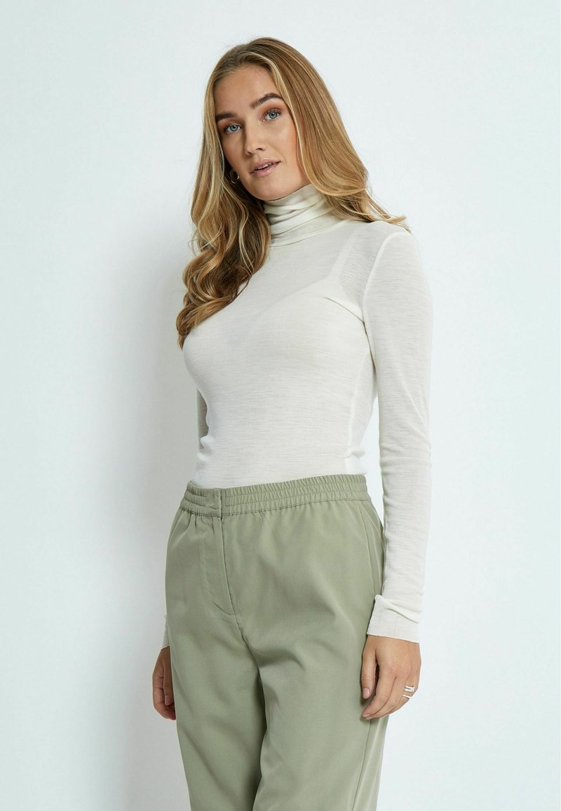 Pikendatud varrukatega heledast kreemjas tooni turtleneck-särk, mis on valmistatud pehmest, õhukesest materjalist, on kombineeritud laia lõikega salve roheliste pükstega, millel on elastne vöökoht.