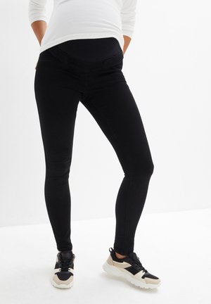 Jeans premaman neri con cintura elastica, slim fit. Abbinati a sneakers nere e crema con suola spessa.