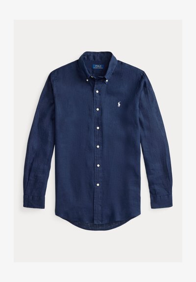 Pusmūksnas zila garo piedurkņu pogājama krekliņa vieglā audumā ar noapaļotu apakšmalu un mazu izšūtu logotipu krūtīs.