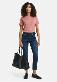 Roze T-shirt met korte mouwen, donkerblauwe jeans, zwarte leren instappers en een grote gestructureerde zwarte tote bag. Weergegeven tegen een witte achtergrond.