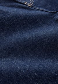 Ciemnoniebieska tkanina dżinsowa z delikatnym połyskiem, charakteryzująca się gładką fakturą oraz subtelnymi różnicami w kolorze i wzorze, ukazująca ciasne splatanie nitki.