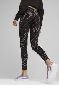 Zwarte legging met een tijgerstreep patroon in grijs. Heeft een hoge taille en is gecombineerd met lichtpaarse sneakers.