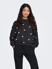 Black sweatshirt with white daisy embroidery, crew neckline, long sleeves, ribbed cuffs and hem, paired with black loose-fitting trousers.