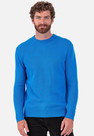 Pull en tricot bleu avec un col ras du cou, manches longues et poignets côtelés. La texture semble douce et lisse. Assorti à un pantalon noir.