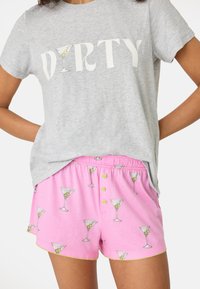 Grå t-shirt med kort ärm som har texten "DIRTY" och en grafik av ett martiniglas. Rosa shorts med ett upprepat mönster av martiniglas och guldkant.