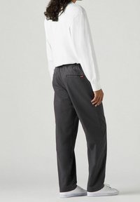 Tmavě šedé kalhoty volného střihu s elastickým pasem a zadními kapsami, zkombinované s bílou košilí s dlouhým rukávem a bílými teniskami.