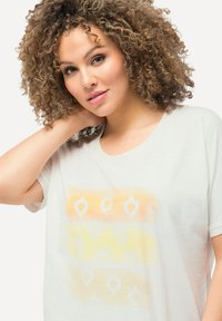 Camiseta beige claro con un suave diseño de degradado colorido en tonos naranja y amarillo, con patrones abstractos en blanco.