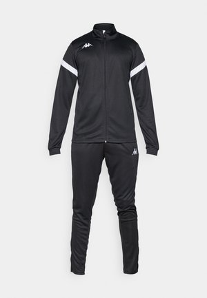 Zwart trainingspak bestaande uit een zip-up jack en tapered broek, gemaakt van een gladde stof met witte zijkanten en een logo op de borst en dij.