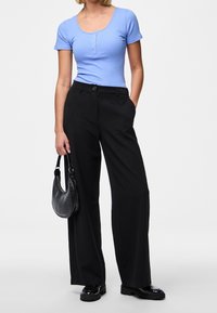 Světle modrý žebrovaný top s krátkým rukávem a detaily s knoflíky, doplněný o černé široké kalhoty s vysokým pasem a černou kabelku.