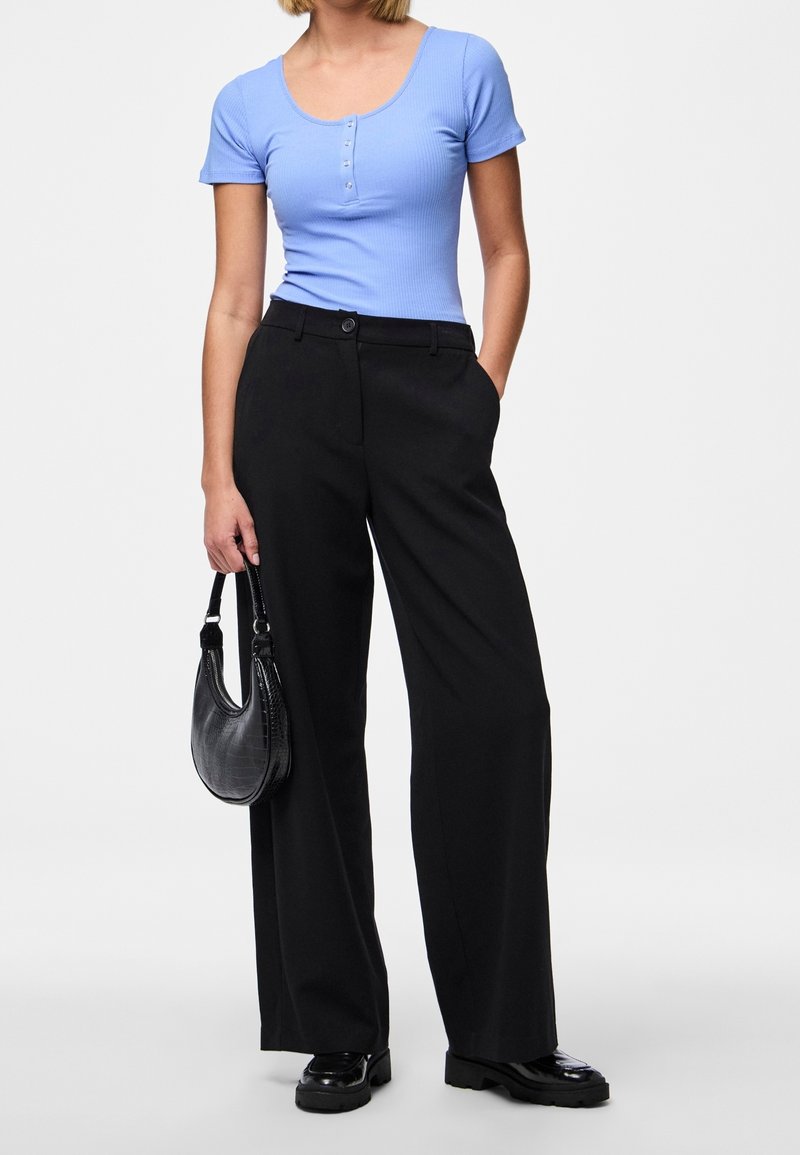Světle modrý žebrovaný top s krátkým rukávem a detaily s knoflíky, doplněný o černé široké kalhoty s vysokým pasem a černou kabelku.