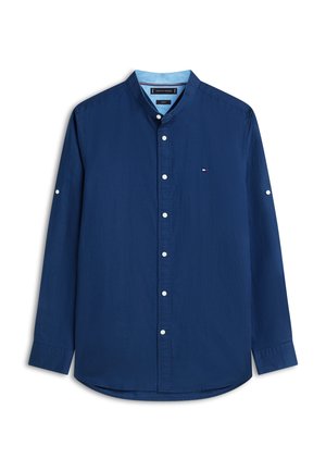 Temno modra srajca z dolgimi rokavi, z gumbi in stoječim ovratnikom, belimi gumbi ter majhnim izvezenim logotipom na prsih.