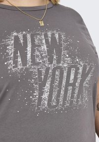 Šedé bavlněné tričko s velkým bílým potiskem "NEW YORK" s efekty rozstřiku. Základní střih s kulatým výstřihem a krátkými rukávy.