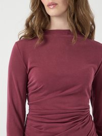 Langdurige jurk van diep bordeauxkleurige stof, met een hoge hals en geplooide details in de taille, wat een textuur effect creëert.