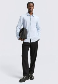 Világoskék hosszú ujjú ing, fekete nadrág és fekete táska. Sima anyag, testhez szabott fazon, gombos gallér és fényes fekete cipők.