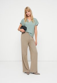 Top v-neck texturat de culoare verde deschis, asortat cu pantaloni largi bej, accesorizat cu o poșetă neagră și tocuri bej cu vârful ascuțit.