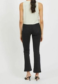 Black flared jeans made of denim, featuring a mid-rise waist and rear pockets. Paired with a grey sleeveless top and black heels.