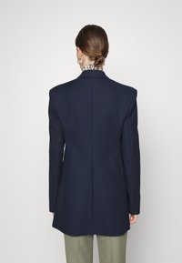 Námořnický oblekový blazer se strukturovaným designem, klopovým límcem, dlouhými rukávy a hladkou texturou; zobrazený ze zadní strany.