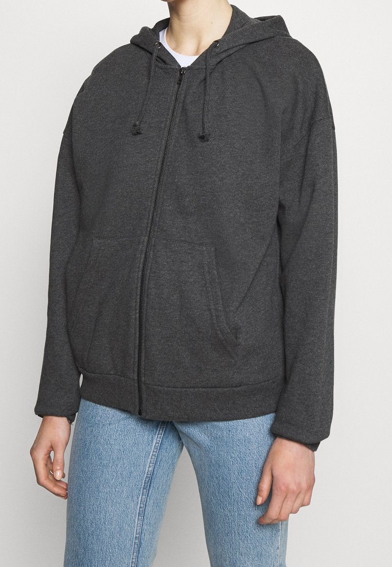 Grijs ritsvest met een trekkoordcapuchon, voorzakken en ribbelboorden. De stof ziet er zacht en gestructureerd uit, geschikt voor casual kleding.
