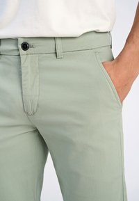 Pantalons slim-fit vert clair en tissu lisse, dotés d'une fermeture à bouton et de poches latérales au design simple.