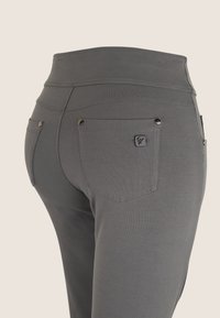 Leggings grises con una cinturilla alta, que cuentan con dos bolsillos traseros con herrajes metálicos y una etiqueta tejida de la marca. Textura suave, forma ajustada.