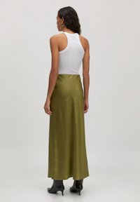 Olijfgroene satijnen maxi-rok gecombineerd met een witte mouwloze top, met een gladde textuur en een stijlvolle silhout. Zwarte haklaarzen maken de look compleet.
