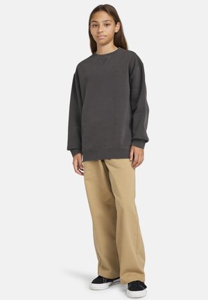 Tmavohnedá mikina s okrúhlym výstrihom a spustenými ramenami, skombinovaná s voľnými béžovými nohavicami. Čierno-biele tenisky dopĺňajú celý outfit.