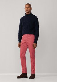 Marineblauwe kabelgebreide coltrui, roze slim-fit broek, bruine leren enkellaarsjes; soepele textuur en contrasterende kleuren.