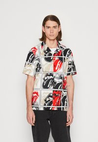 Camisa de manga corta con un atrevido patrón gráfico en colores rojo, negro y beige, fabricada con material ligero y un corte relajado.