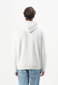 Lys grå hoodie lavet af blødt stof, med en stor hætte, ribbede ærmer og talje. Båret sammen med lyseblå denimjeans.