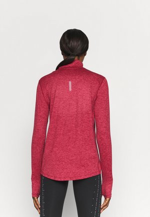 Haut de sport rouge à manches longues avec un col montant, en tissu texturé et avec des bandes réfléchissantes au dos. Associé à des leggings noirs avec des accents.