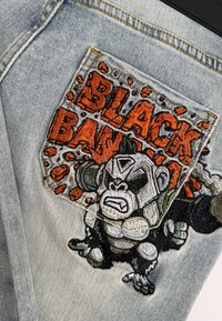 Lichtblauwe denim met een grote geborduurde patch met een gorillapersonage en de tekst "BLACK BAN" in oranje en zwarte tinten.